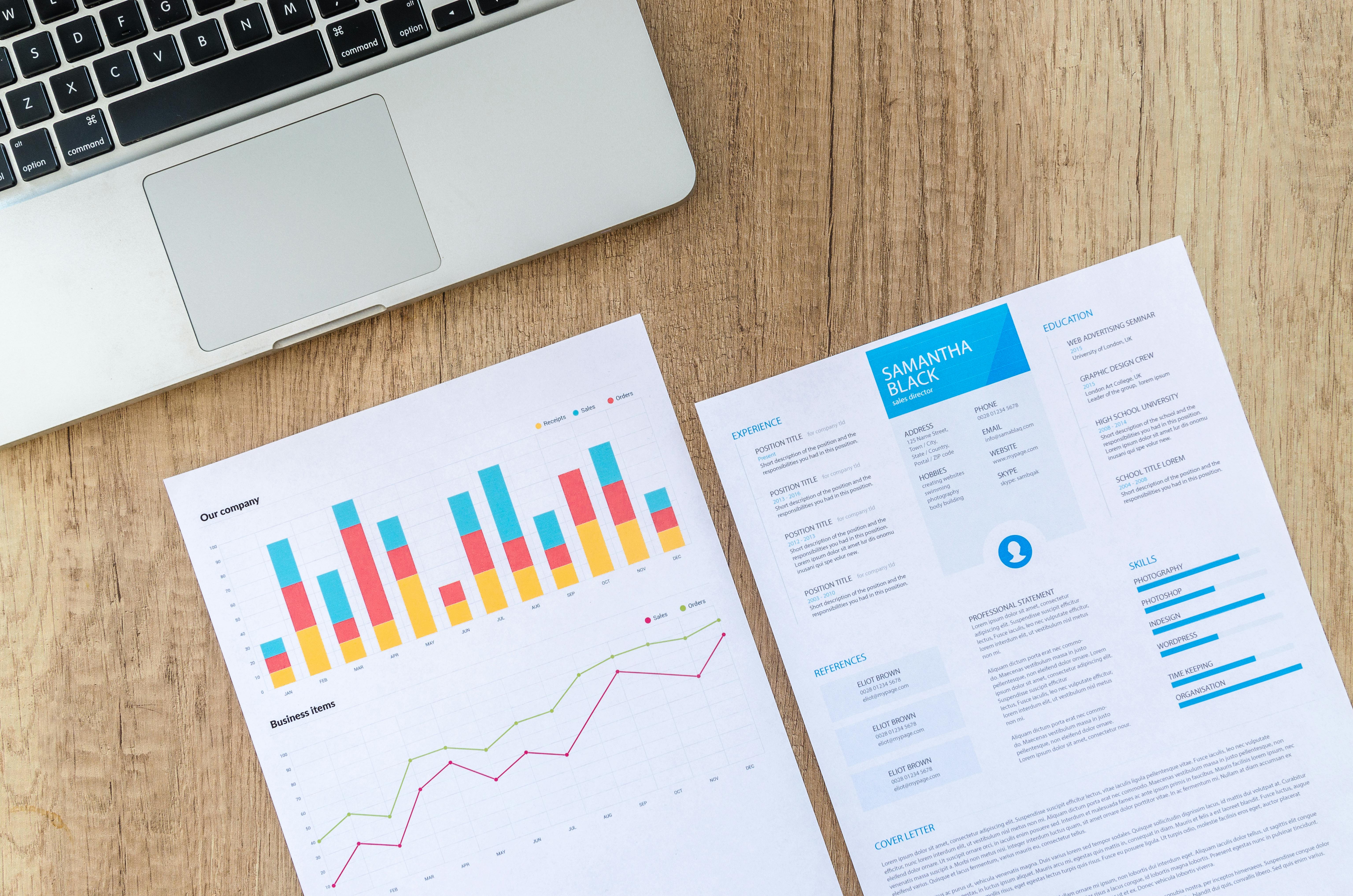 Two pieces of paper with charts on one and a resume on the other next to a computer